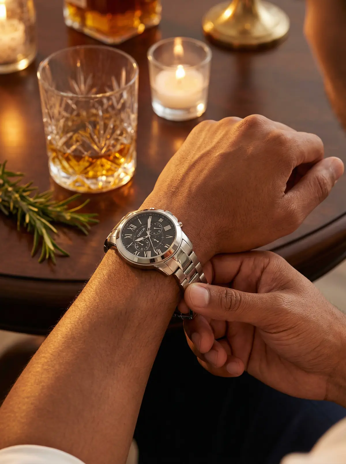 Close-up: hand adjusting watch, cocktail glass and candle flame in soft bokeh.